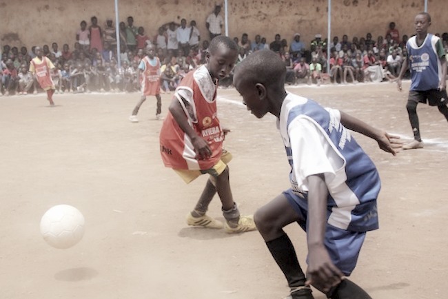 Fußballspielen und Lernen: Das Prinzip der Ayiera-Initiative. - Zwei Jungs kämpfen auf einem Sandplatz um einen Ball. Foto © Tom Rübenach